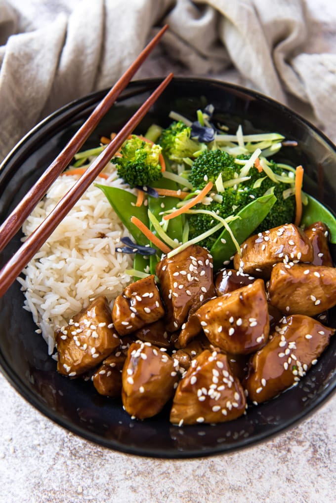 Close up overhead shot of a bowl with teriyaki chicken, vegetables and rice and chopsticks