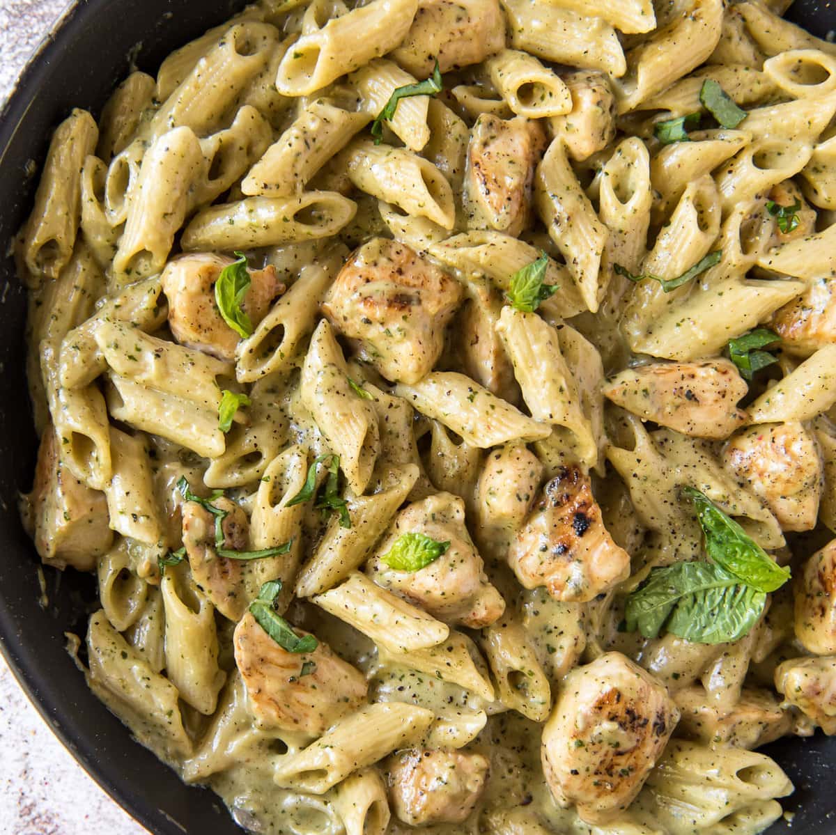 A pan filled with Chicken and Pasta, topped with a creamy pesto sauce.