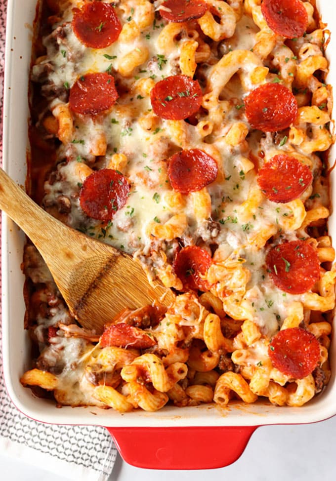 overhead shot of spoon in casserole dish with pasta, sauce and pepperoni.