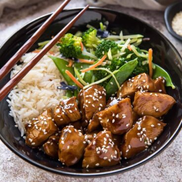 A bowl of teriyaki chicken, white rice, salad, and chopsticks.