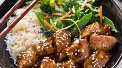 A bowl of teriyaki chicken, white rice, salad, and chopsticks.
