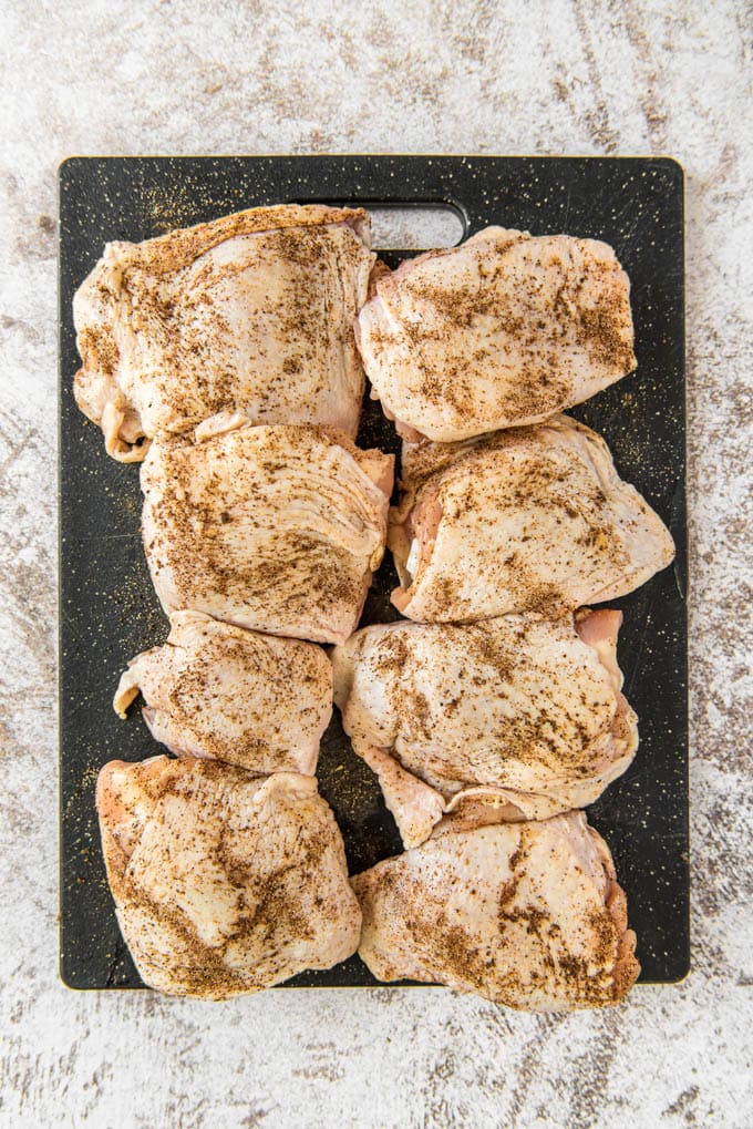 8 raw chicken thighs with seasoning on a cutting board.