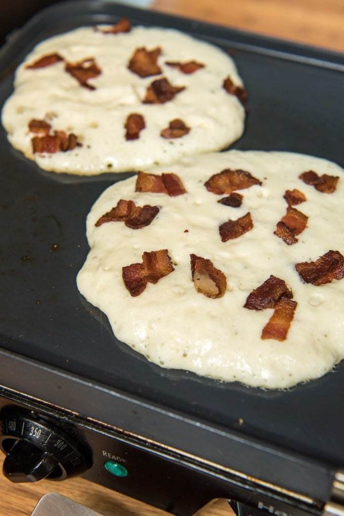 Pancake batter cooking on a griddle, topped with bacon