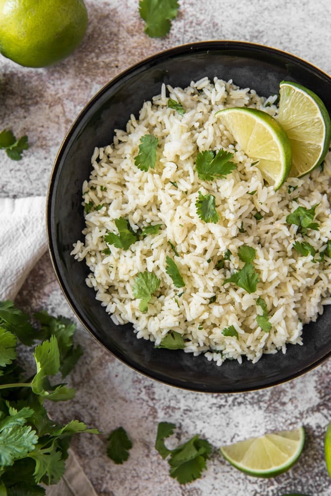 an overhead shot of a bowl of rice with cilantro and lime wedges