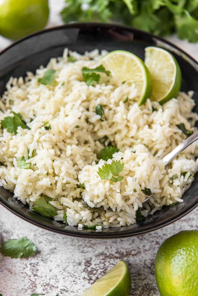 a bowl of rice with cilantro and limes, with a spoon lifting up a bite.