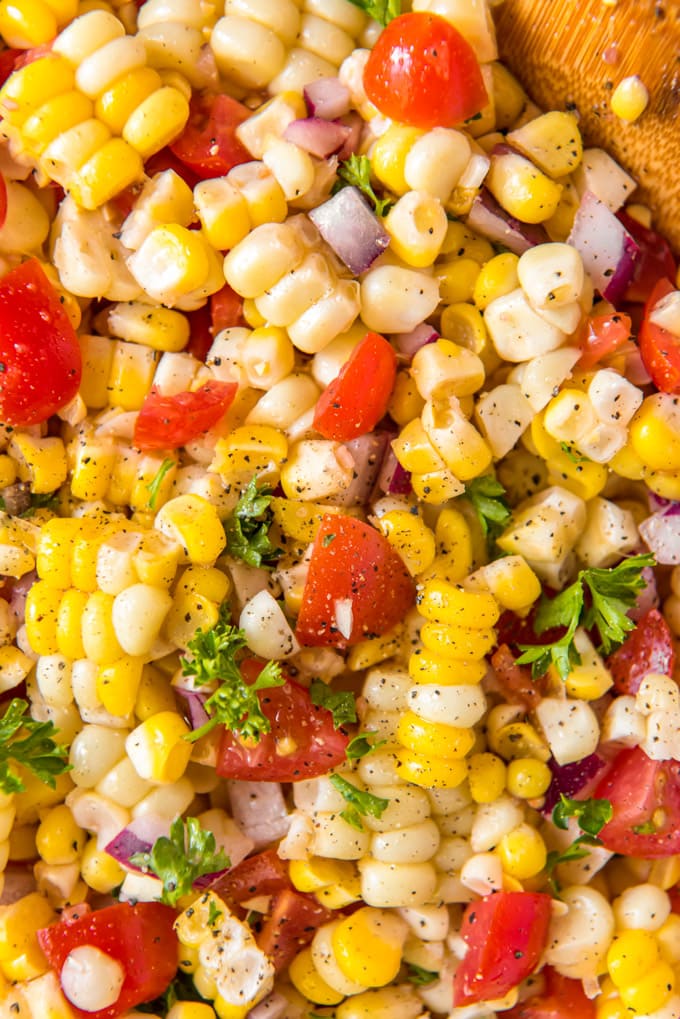 a close up of a corn salad with tomatoes and onions.