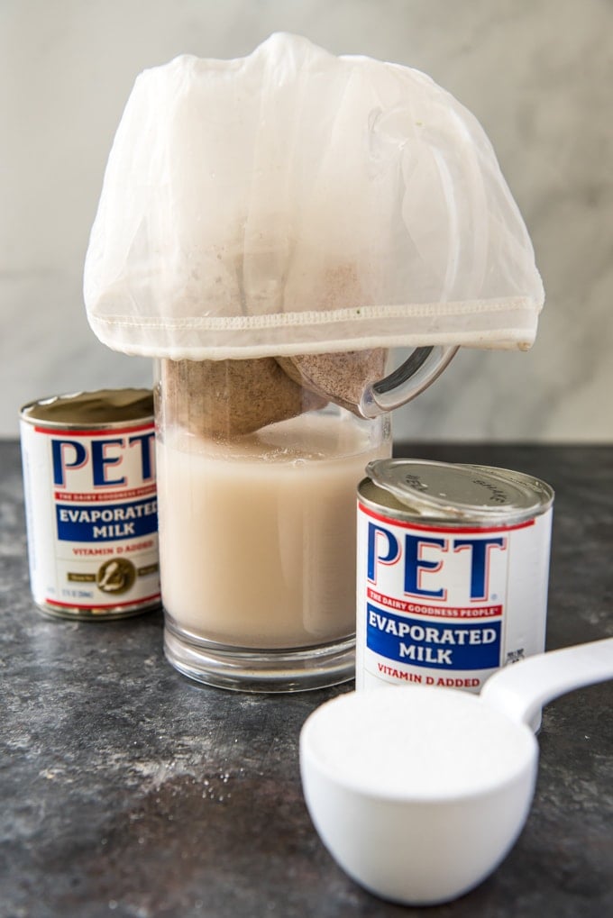 a pitcher with rice and cinnamon being strained through a mesh bag.