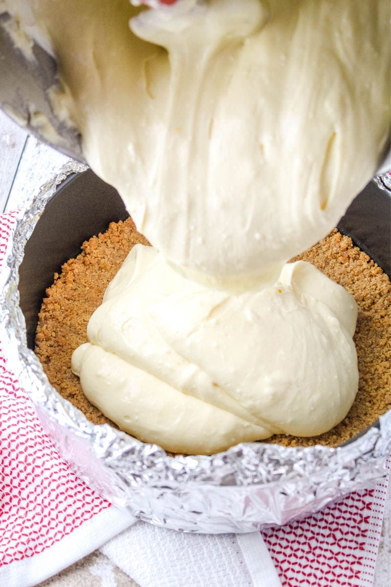 cheesecake batter being poured into a springform pan with a graham cracker crust