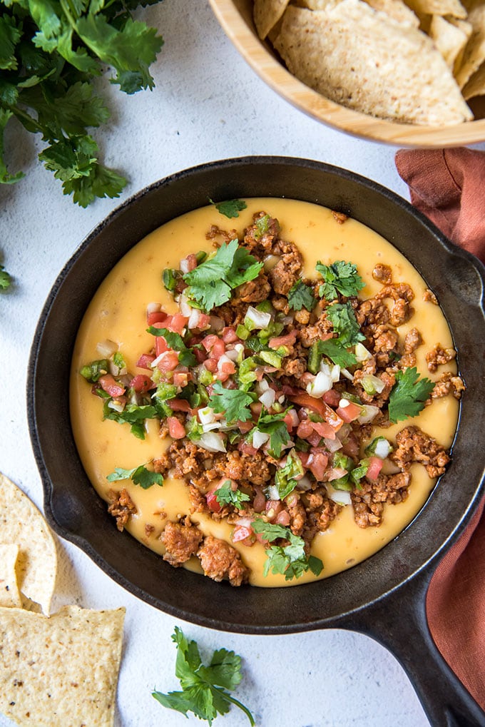 an overhead shot of a cast iron skillet with queso fundido cheese dip topped with chorizo and pico de gallo.