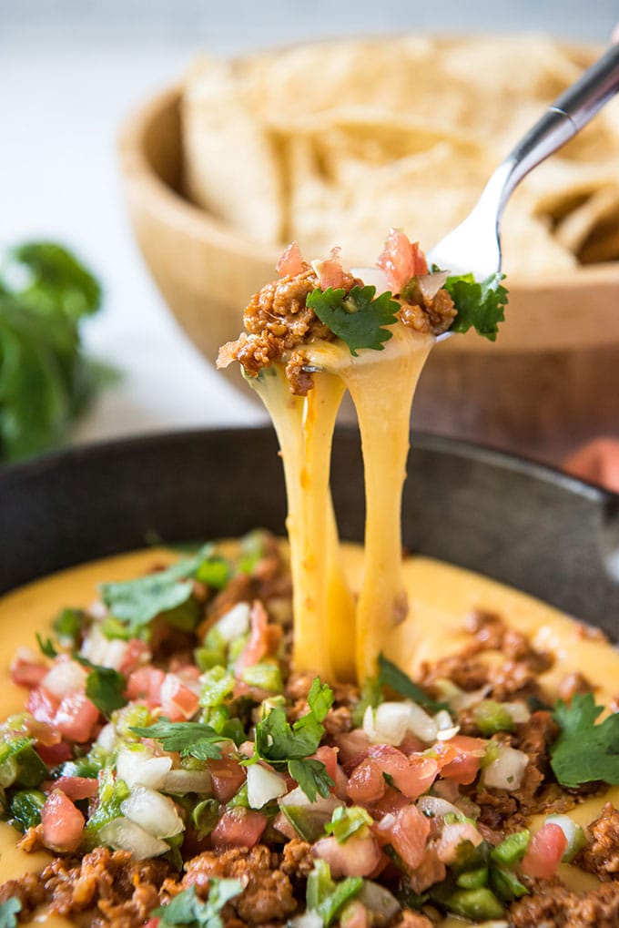 a fork lifting stringy yellow cheese from a pan of queso fundido