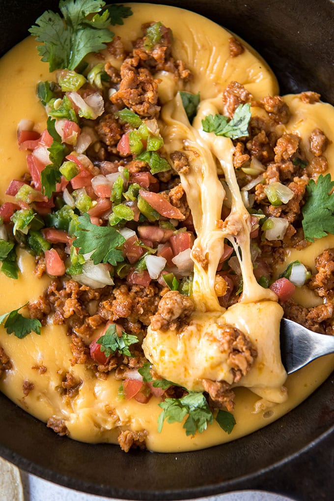 cheese dip with choizo and pico de gallo on top in a cast iron skillet with a fork pulling cheese for a serving