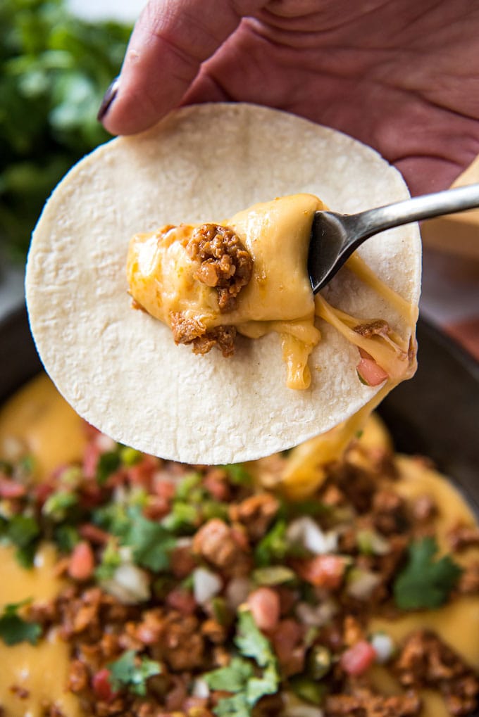 a hand holding a tortilla and a fork scooping cheese and chorizo onto the tortilla.