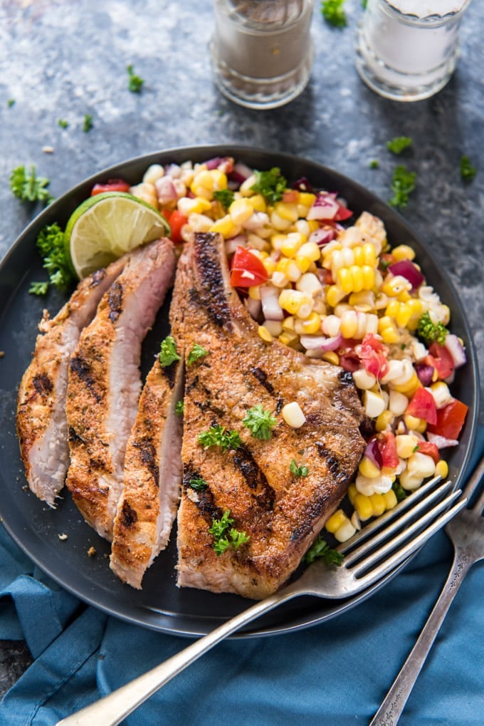 A grilled pork chop on a plate, sliced, with some corn salad on the side.