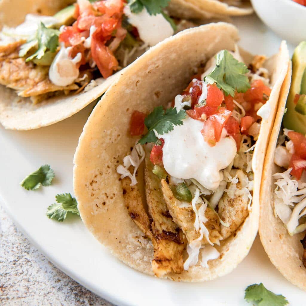 A close up of grilled fish tacos with sour cream, tomato, and cilantro
