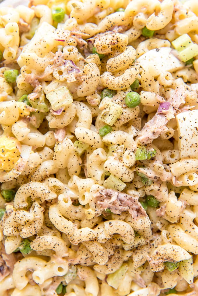 A close up image of tuna macaroni salad with peas, onions and macaroni.