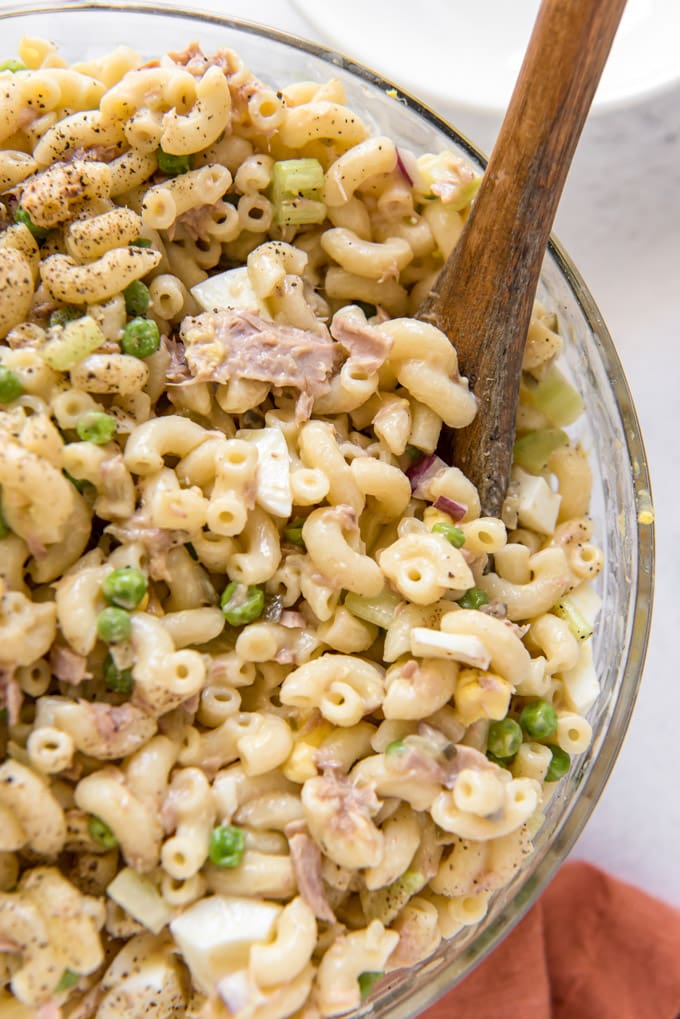 macaroni, peas, onions and tuna in a large glass bowl with a wooden spoon
