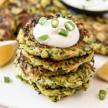 Stack of zucchini fritters with sour cream and green onions on top