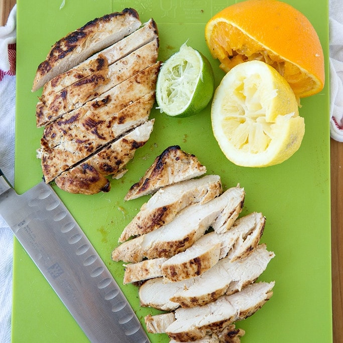 slice chicken breast, squeezed orange, lime and lemon, knife, green cutting board