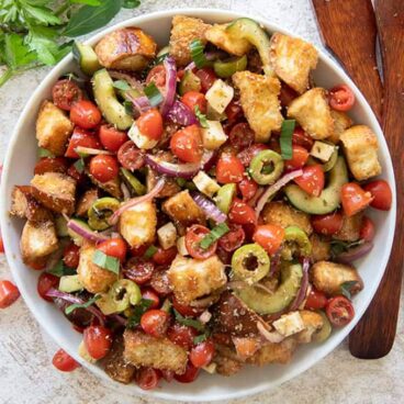 a white bowl with bread and vegetables salad, wooden spoons, basil.