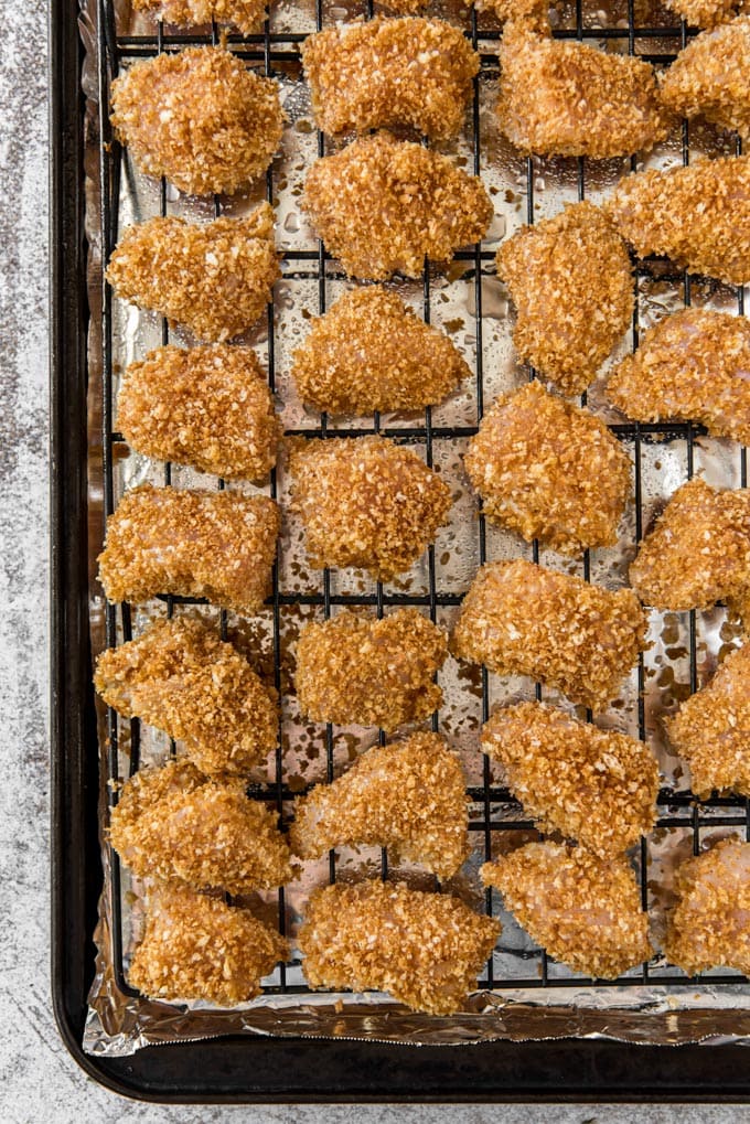 a black wire rack, over foil on a baking sheet with chunks of breaded chicken on top.