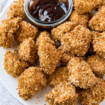 Breaded and baked chicken nuggets with small dish of barbecue sauce.