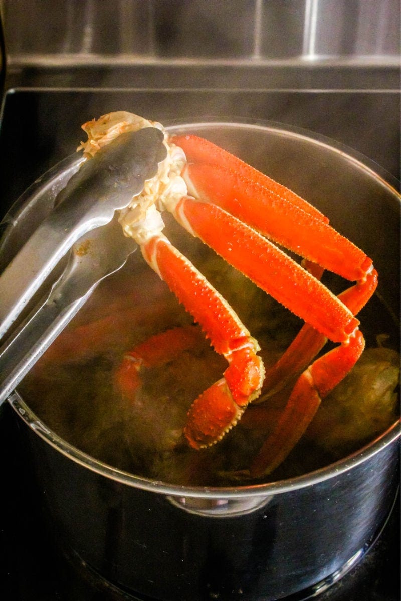 Making crab legs is easier than you think! Ready in only 5 minutes, these crab legs are the best way to treat yourself to a fancy meal at home! tongs lifting crab legs out of a pot of water