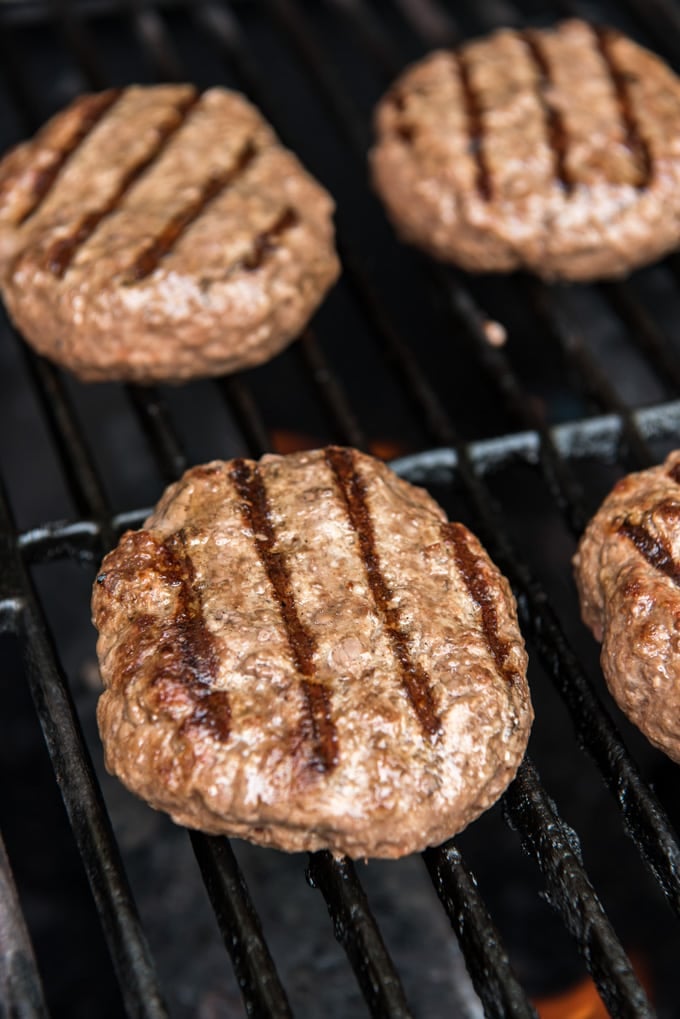 Four ground beef patties with grill marks, sitting on grill grates.