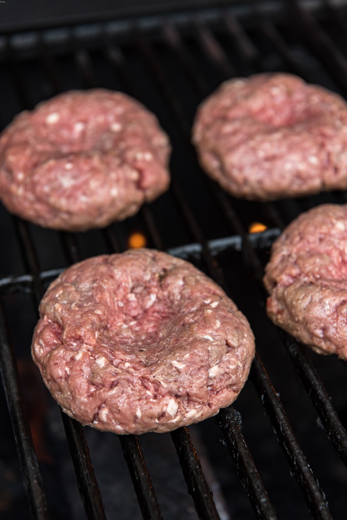 four ground beef burger patties with an indent in the center, sitting on grill grates.