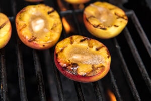 3 peach halves cut side up with grill marks, sitting on a grill.