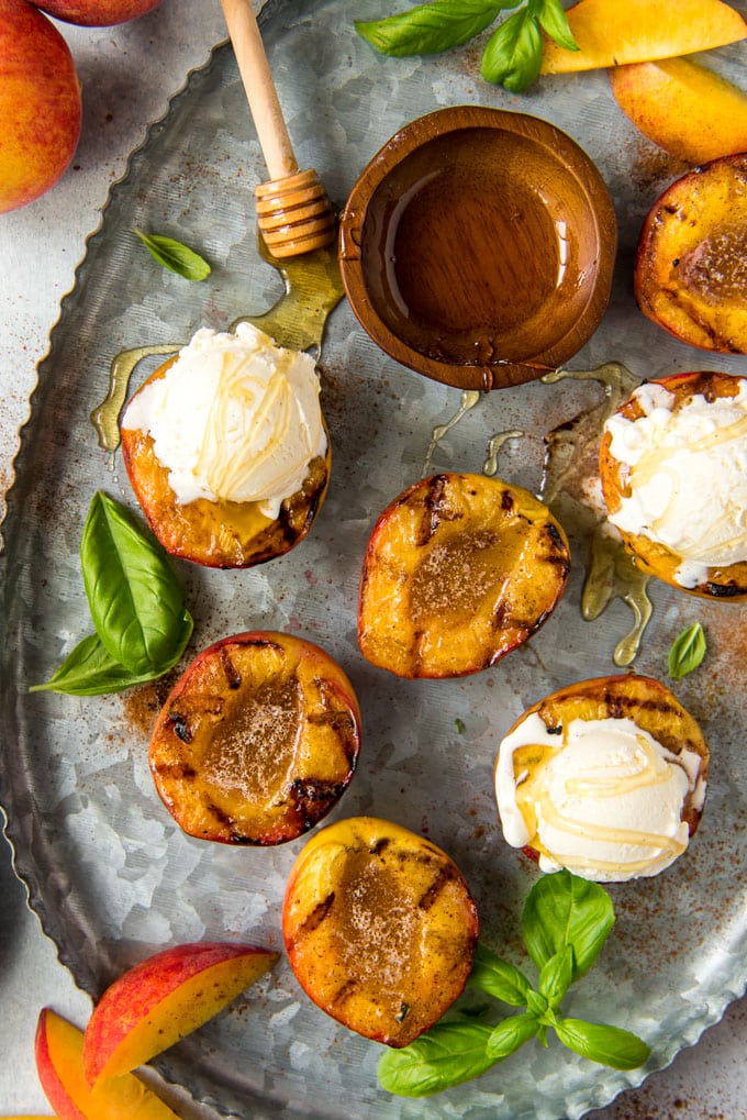 a galvanized tray with 6 grill marked peach halves, 3 with vanilla ice cream and the others topped with melted cinnamon butter