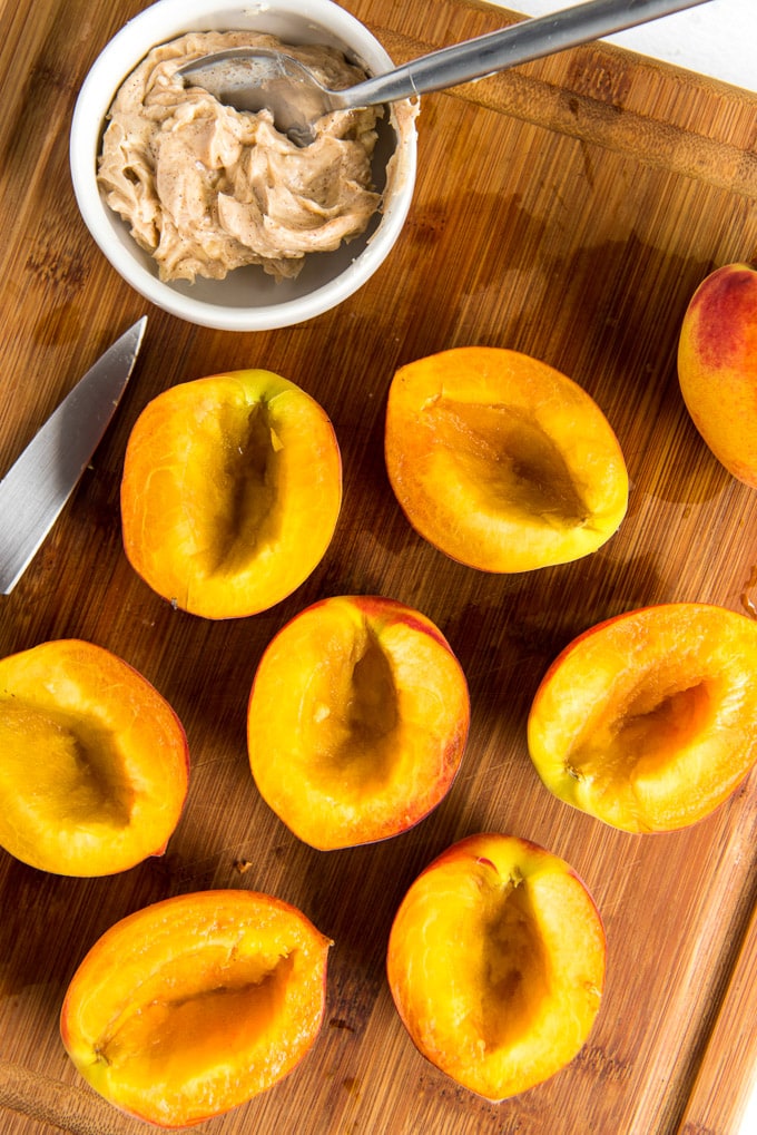 7 peach halves, pits removed, sitting on a wooden cutting board. A small white bowl with cinnamon honey butter.