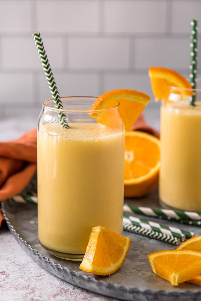 A glass of orange smoothie with straw and fresh orange slices.
