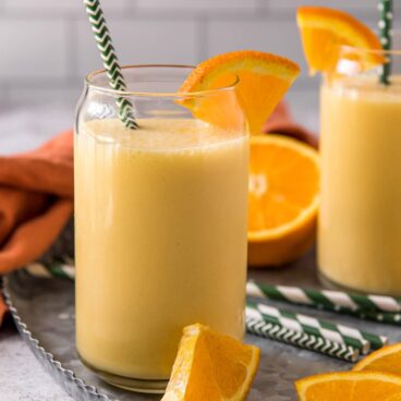 Orange smoothie in a glass with straw and slices of fresh oranges.