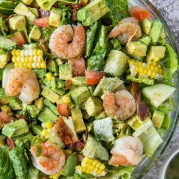 A bowl of salad, with shrimp, corn, and avocado.