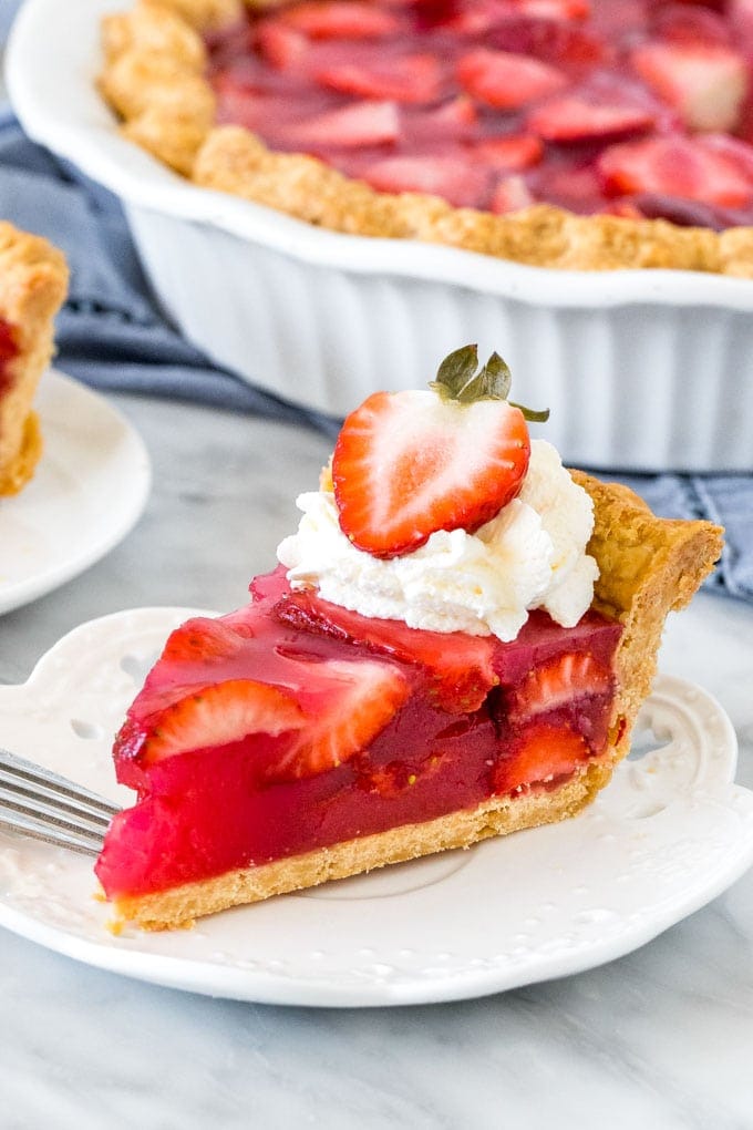 Slice of strawberry pie with whipped cream and a strawberry on top. 