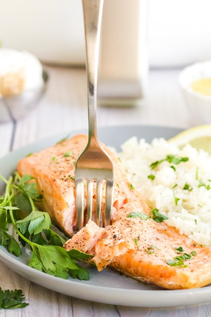 Air fryer salmon with a fork in it with rice and herbs surrounding it on the plate. 