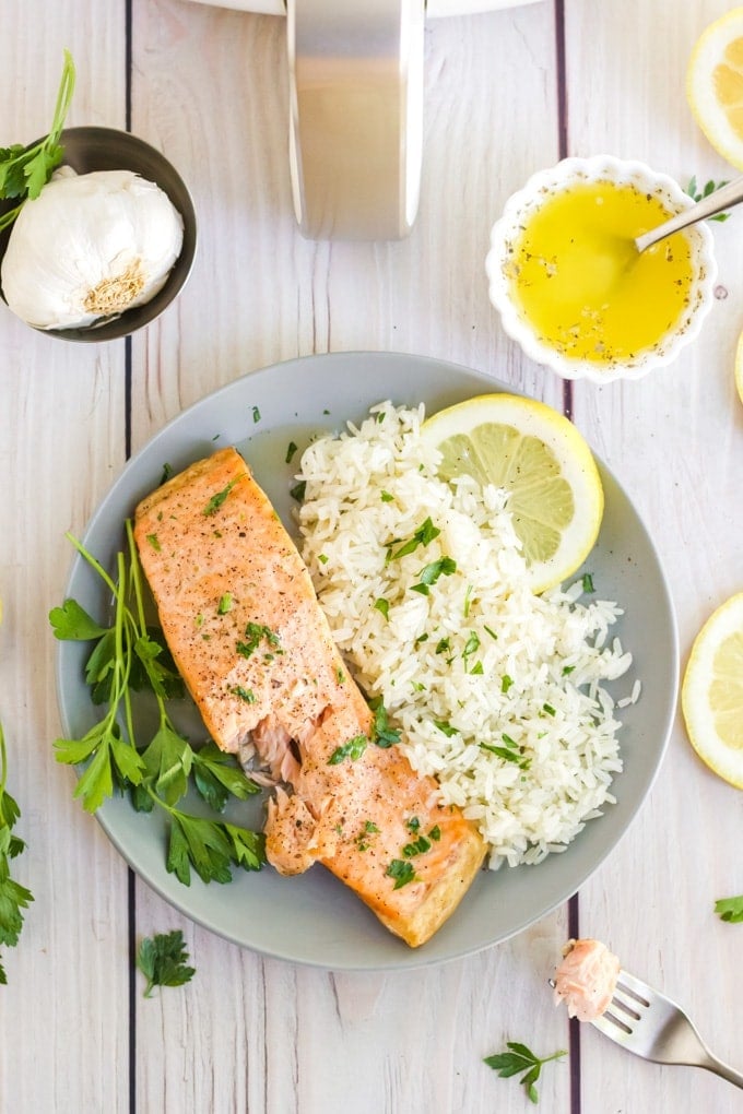 Overhead image of air fryer salmon next to a bed of white rice and garnished with fresh herbs