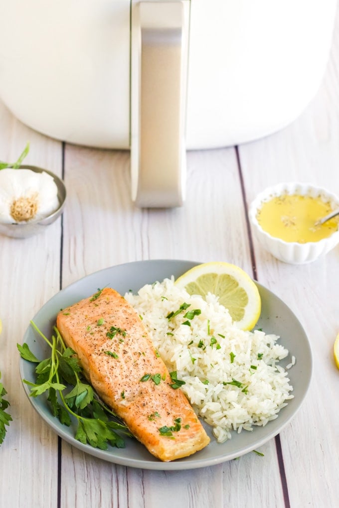 Air Fryer Salmon on a grey plate with white rice and a white air fryer in the background. 