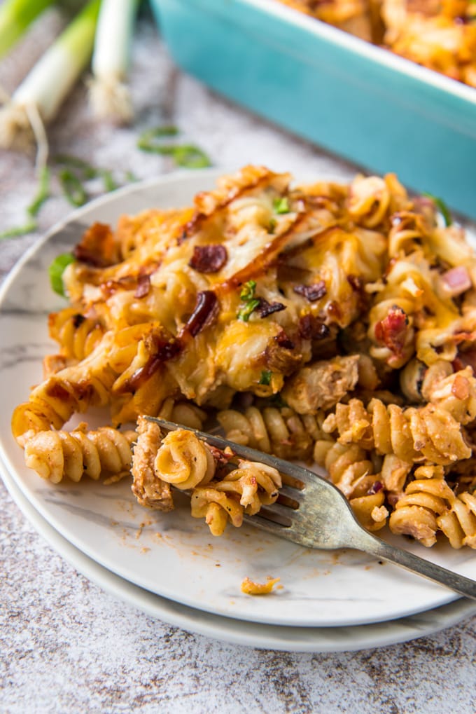 a blue baking dish, white plates with pasta, chicken, bacon, cheese and chicken, a for, green onions