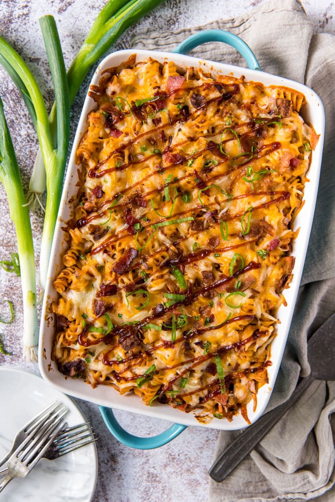 green onions, a white dish with pasta, chicken and bbq sauce, forks, white plates, a gray napkin