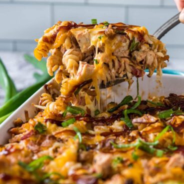 A spoonful of rotini pasta with cheese and barbecue chicken.