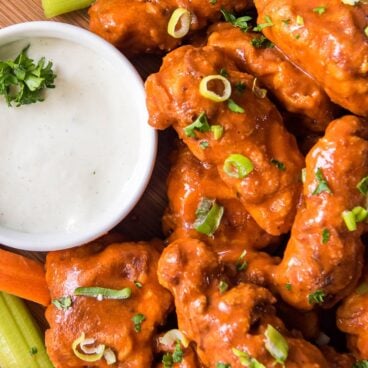 Wings covered in buffalo sauce and a dish of blue cheese dressing.