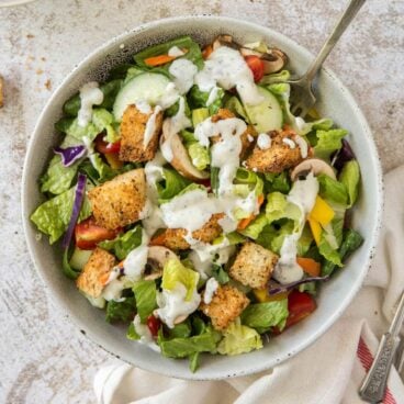 A bowl of salad with ranch dressing.