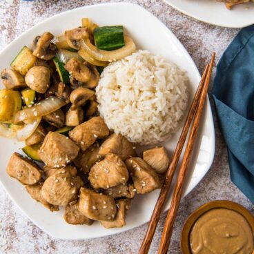 A plate of chicken, vegetables, and white rice, with chopsticks.