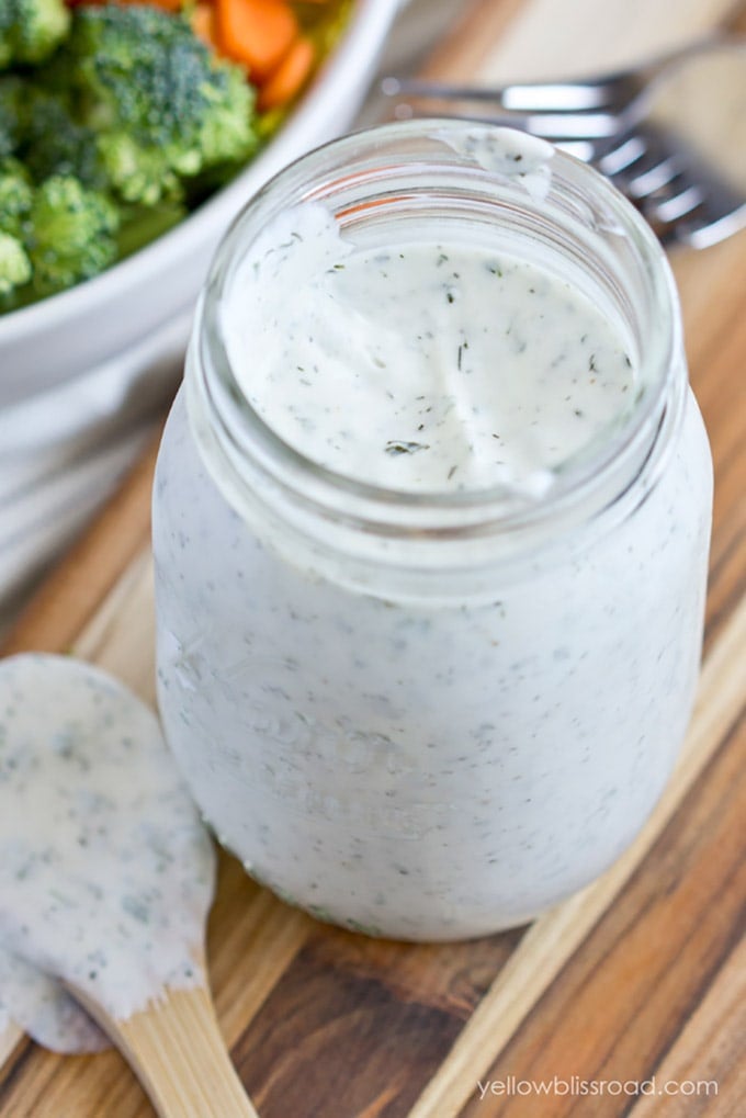 close up of a mason jar with ranch dressing, a wooden spoon and a wood background. 