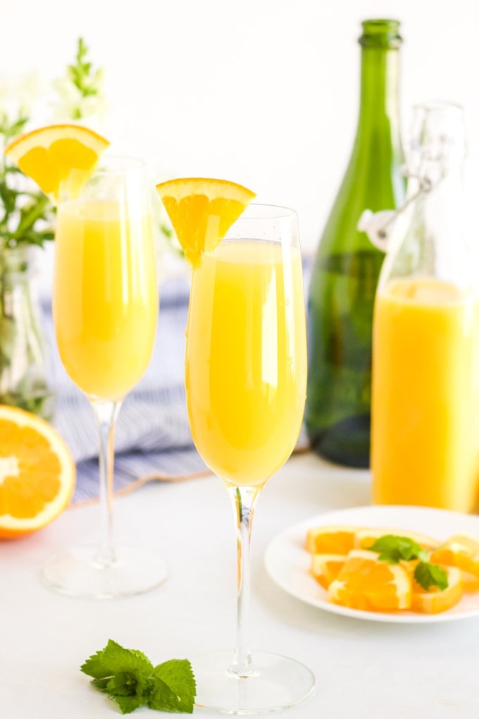 A traditional mimosa with oranges, orange juice and sparkling wine in the background.