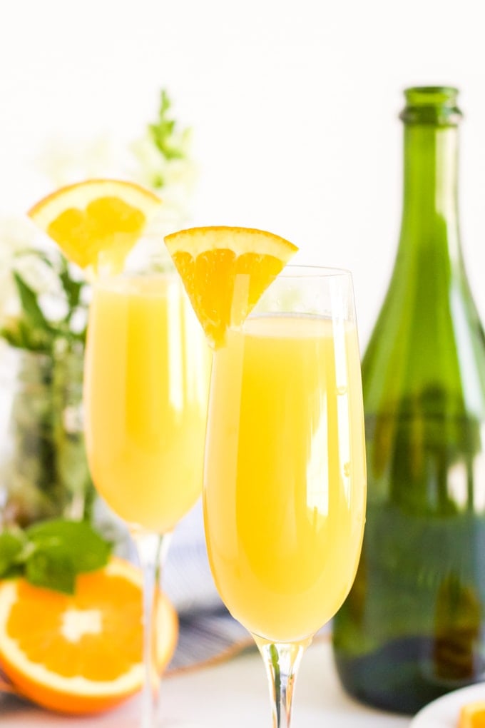 Two glasses of traditional orange juice cocktails with a sparkling wine bottle in the background. 