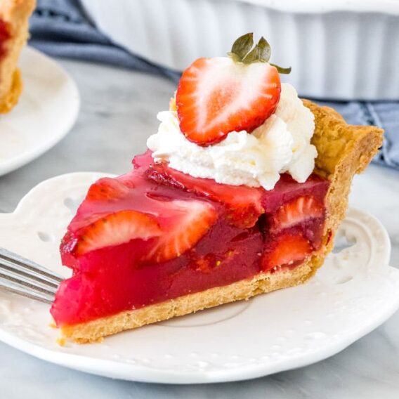 A piece of strawberry cake on a plate, with whipped cream and a fresh slice of strawberry.