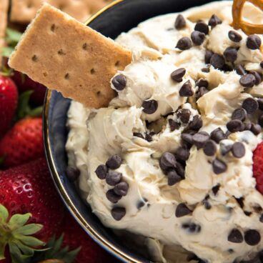 A close up of cookie dough dip with chocolate chips and graham cracker for dipping.