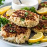 A plate of crab cakes, with lemon wedges.